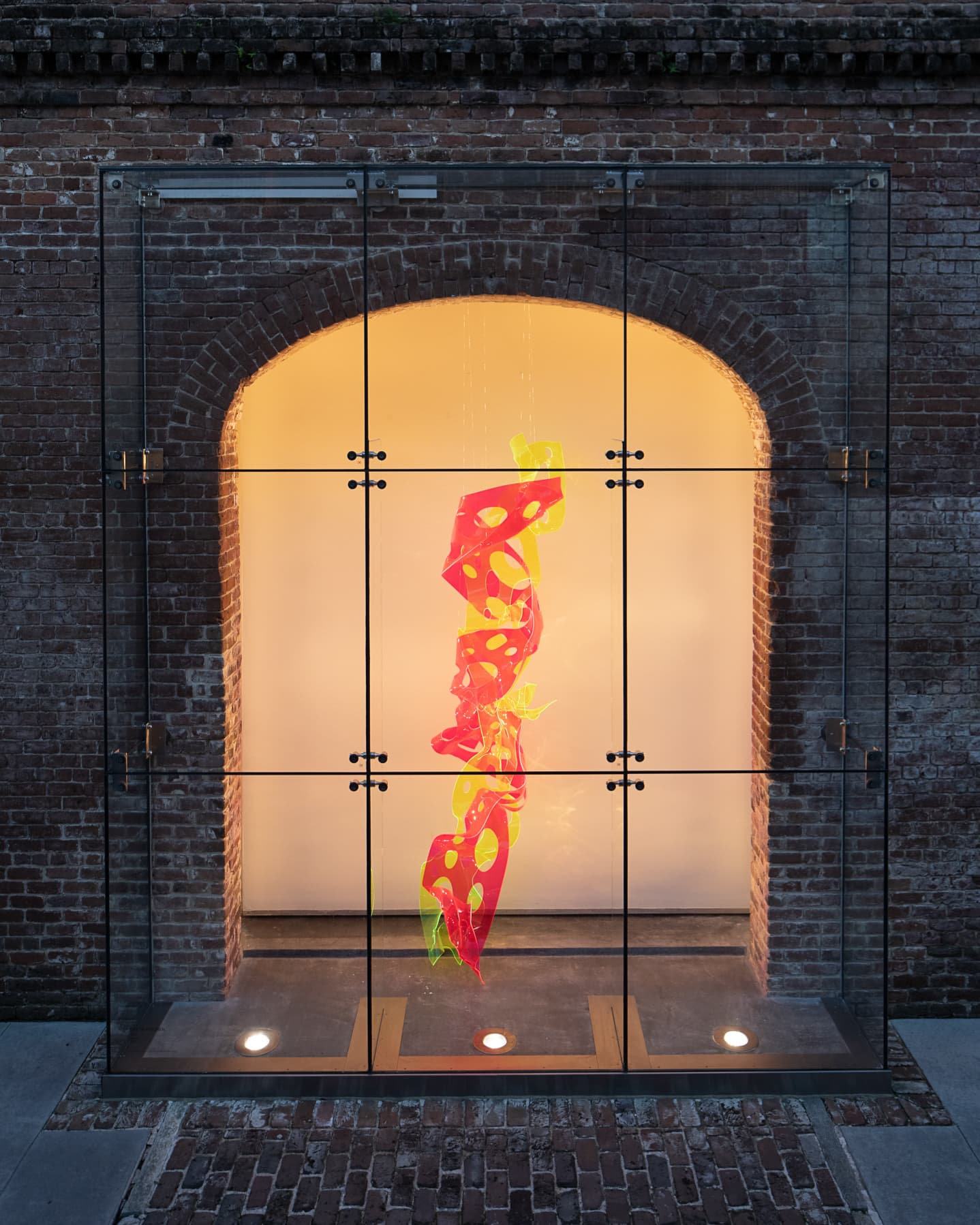 Bright red and yellow abstract sculpture displayed inside a glass exhibition bay — before retouching