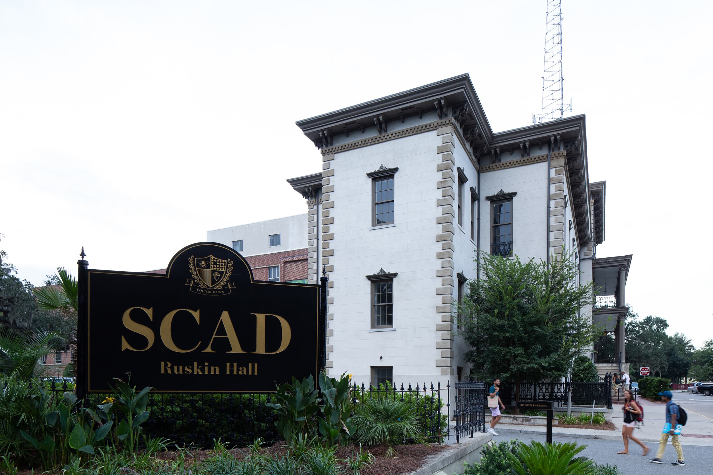 SCAD Ruskin Hall exterior with campus sign, landscaping, and pedestrians — before retouching